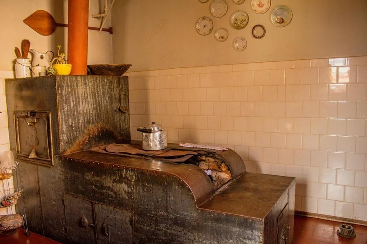 Fogão antigo de ferro na cozinha do casarão, com pratos decorativos na parede de azulejos