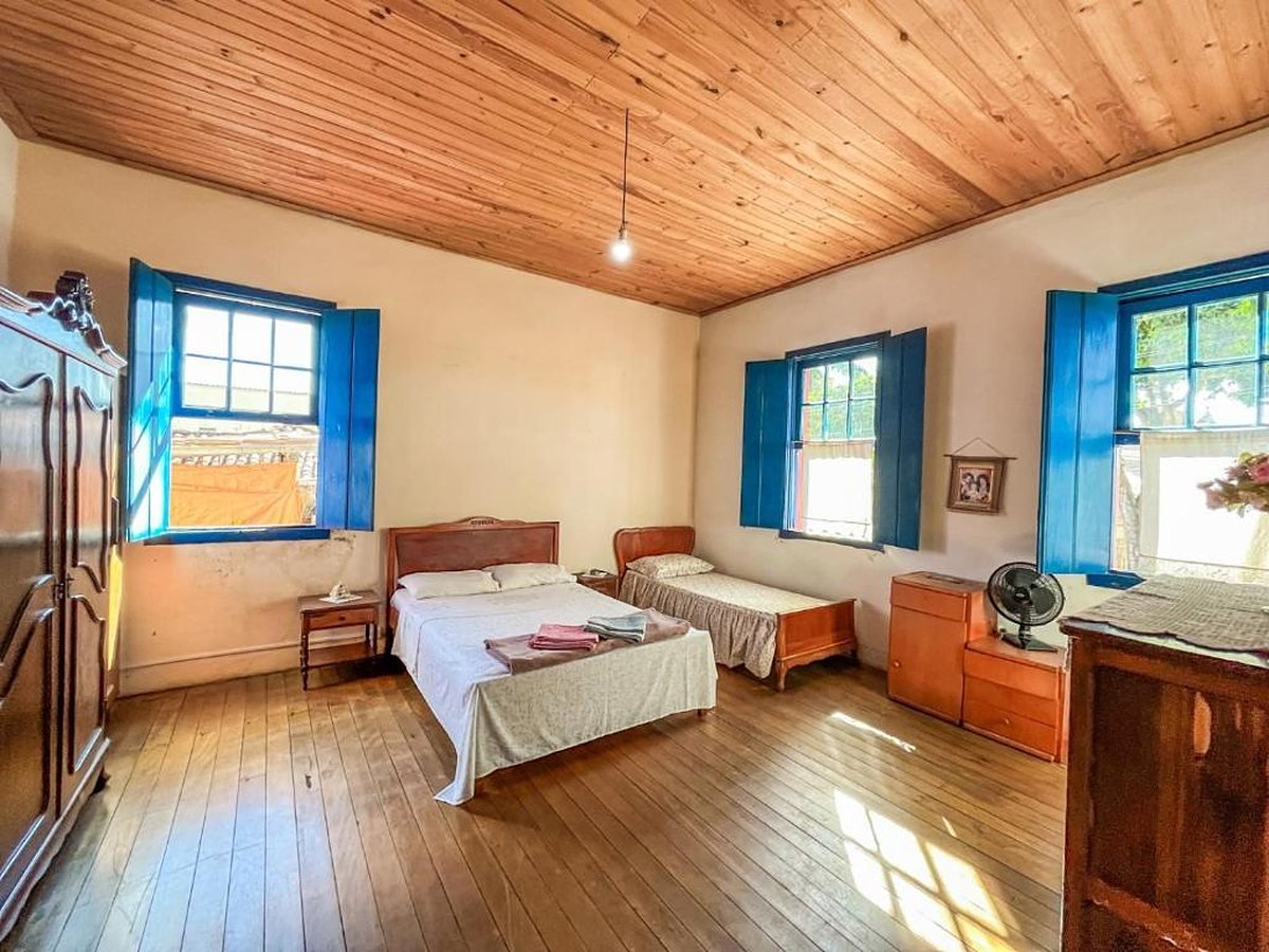 Quarto com cama de casal e de solteiro, janelas azuis e piso de tábuas