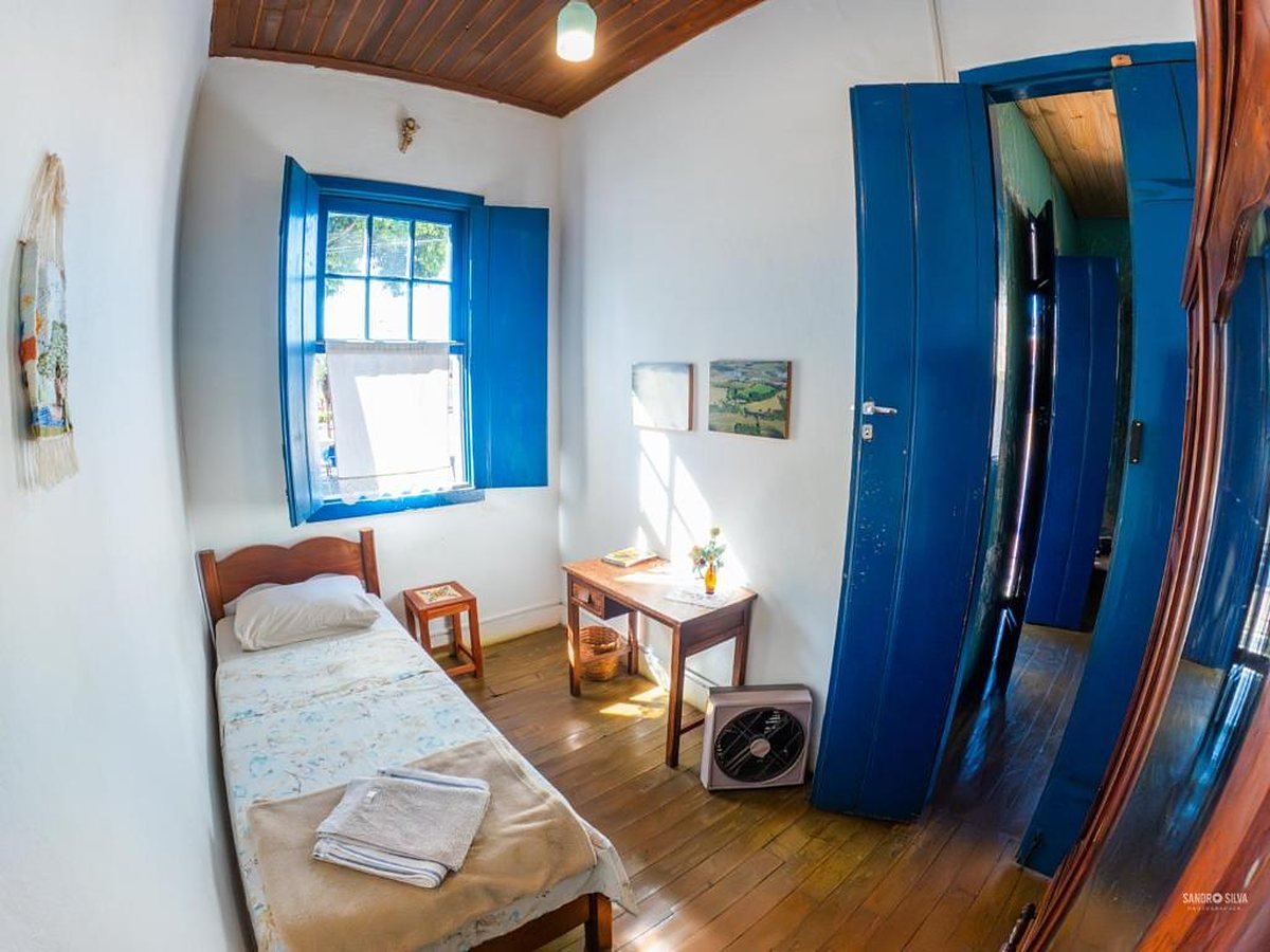Quarto com cama de solteiro, mesinha de madeira e portas duplas azuis