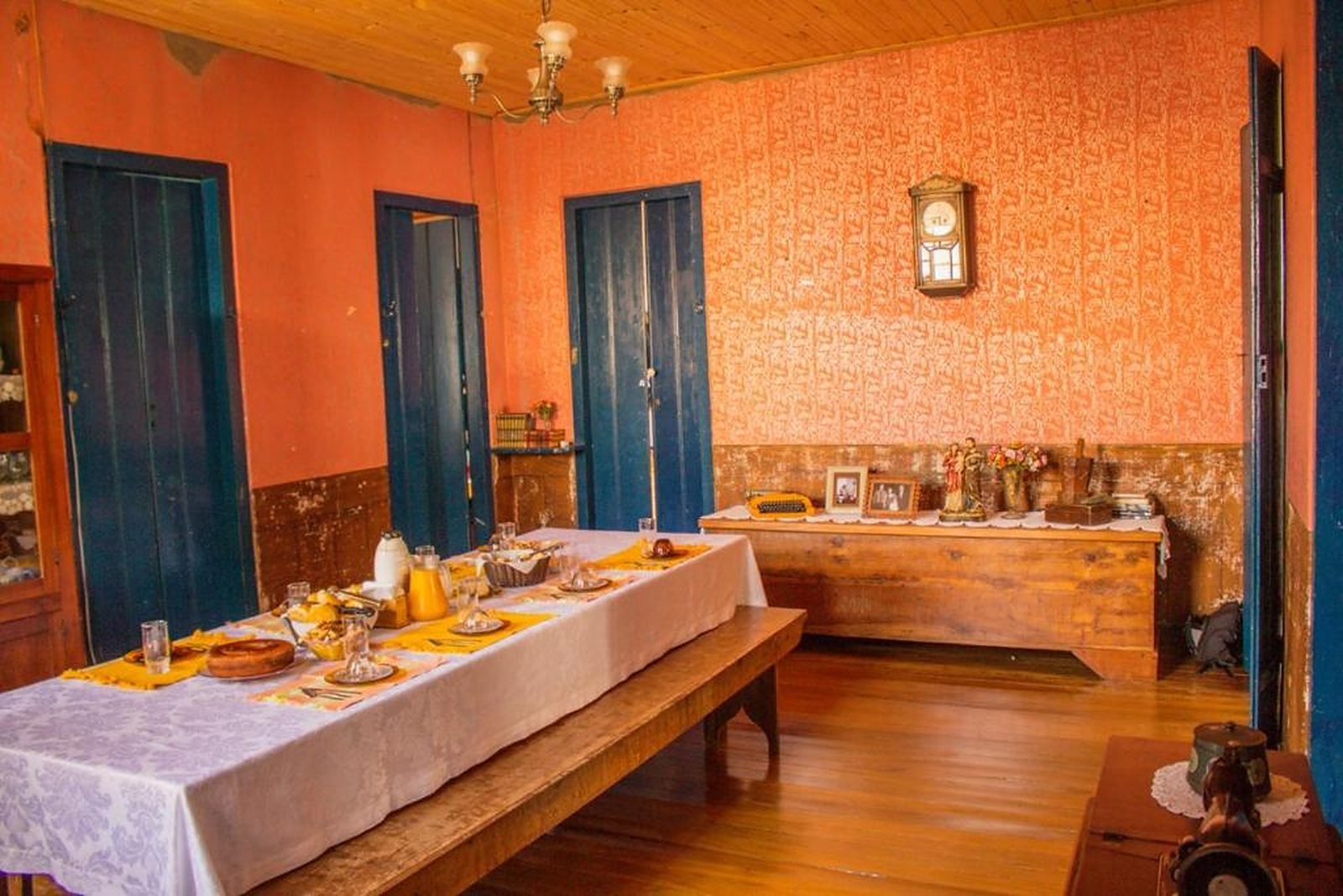Sala do café da manhã com mesa posta, paredes alaranjadas e portas azuis